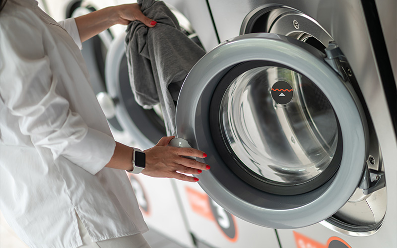 Woman loading clothes into a commercial washing machine.